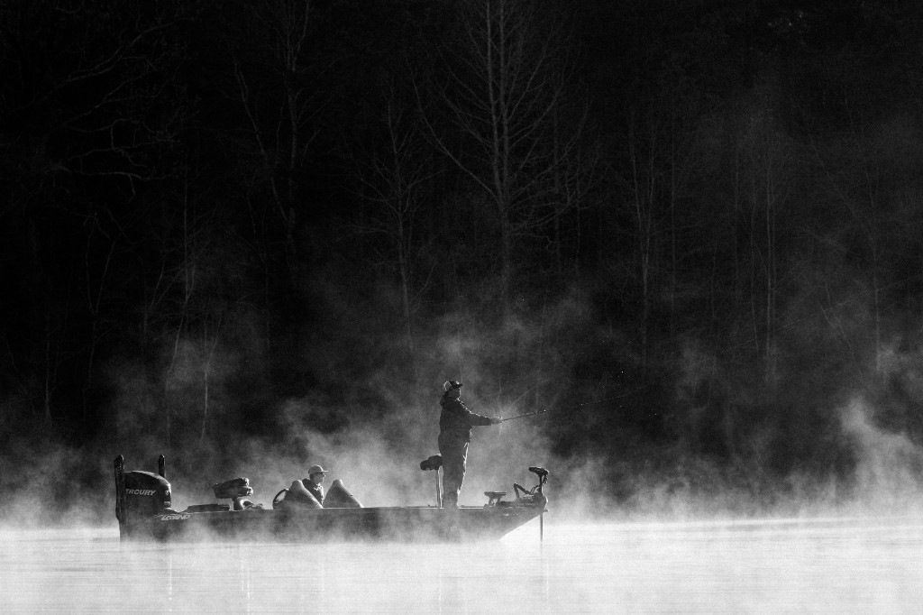 Anglers fishing from a boat in cold, misty dam water